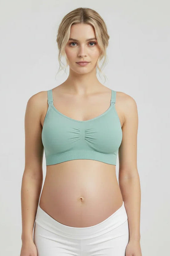 Woman wearing a green sports bra and white pants on a plain background
