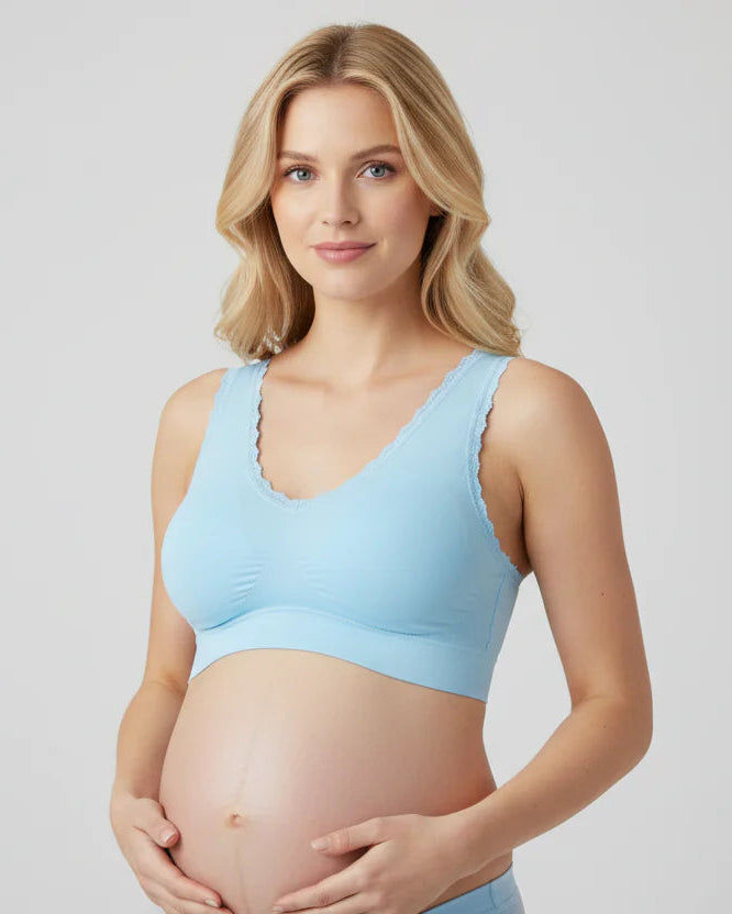 Pregnant woman wearing a light blue maternity sports bra on a plain background