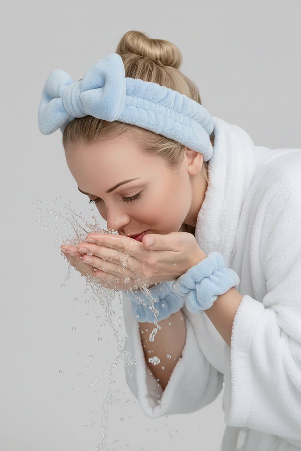 Woman wearing a gray headband with a bow and white robe, holding her face.