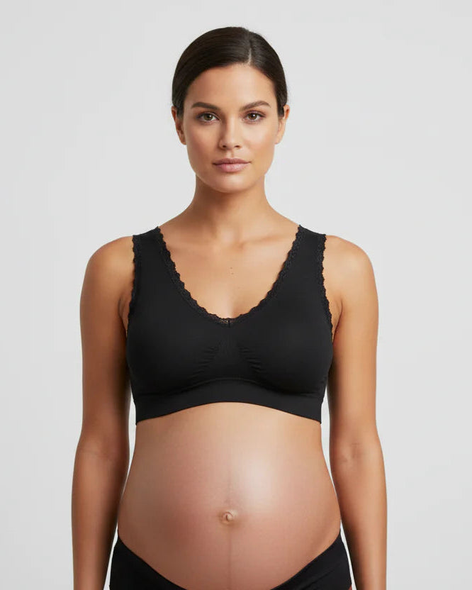Pregnant woman wearing a black maternity bra against a plain background