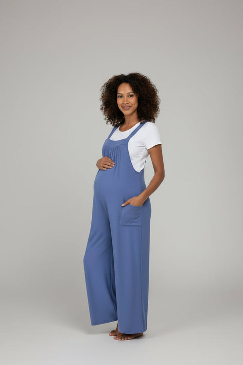 Woman wearing a blue jumpsuit over a white shirt on a plain background